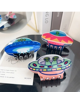 Detailed view of three creative UFO-shaped acrylic hair claws on a sleek black surface