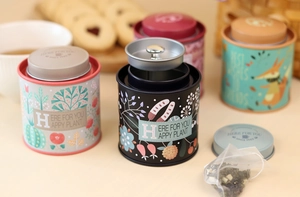 Detail of round tin canisters with double lids showing floral and fox illustrations