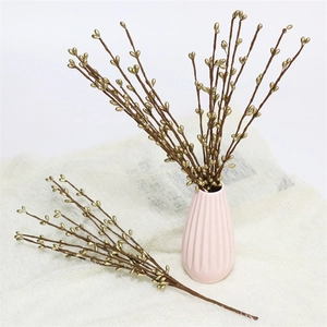 Artificial gold berry branches in a pink ceramic vase on white textured background