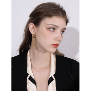 Detail of long gold tassel earrings and thin necklace worn on a fashion model