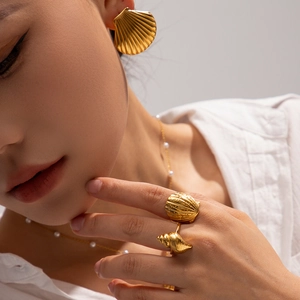 Detail shot of golden shell earrings and ring set worn by a model for a beach-style look