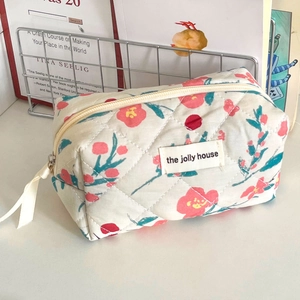 Close-up of floral quilted fabric makeup bag with red flowers and beige label on white surface