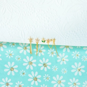 Close-up of gold flower earrings set with zircon, pearls and green leaves on floral background