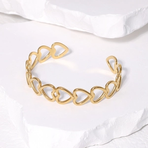 Detailed close-up of gold hollow heart-shaped open bangle on white stone texture