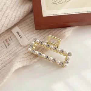 Elegant gold hollow hair claw clip with pearls and rhinestones on a knitted backdrop