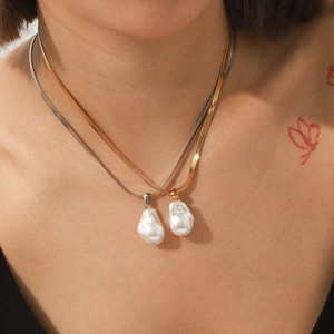 Gros plan de chaînes serpent or et argent avec pendentifs perles baroques sur modèle