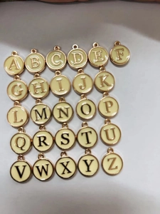 Flat lay of 26 round golden alloy alphabet pendants with beige enamel finish and dark letters