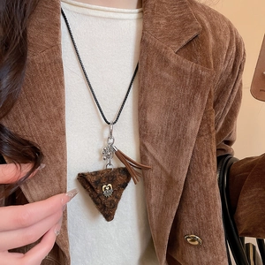 Detail of brown fuzzy triangle pendant with metal tassel on a black sweater chain