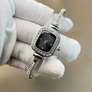 Detailed view of silver square watch with rhinestone bezel held by a gloved hand