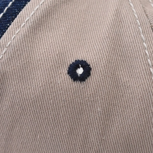 Macro shot of a blue embroidered eyelet and white stitching on a washed khaki baseball cap