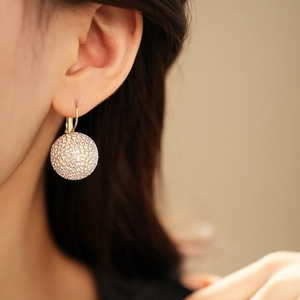 Close-up of luxury gold hook earring with a sparkling crystal-covered sphere on ear