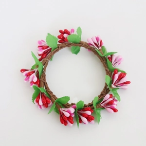 Macro detail of artificial candle ring featuring red pink floral buds and green leaves