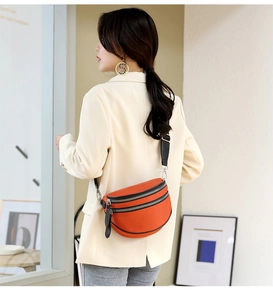 Close-up of orange leather crescent bag with adjustable black strap worn by a model