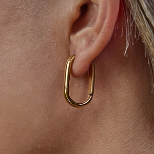 Close-up of elegant gold oval hoop earrings made of titanium steel on a model