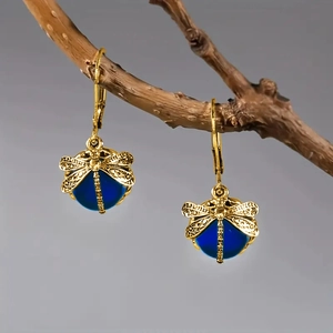 Makroaufnahme goldener Libellen-Ohrringe mit tiefblauen Perlen auf einem Naturzweig