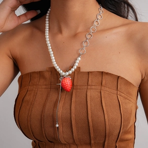 Detailed close-up of asymmetric pearl necklace with red strawberry pendant and silver rings