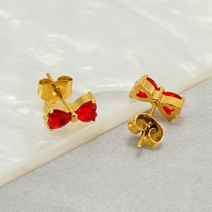 Elegant gold stainless steel bow earrings with red heart stones on marble background