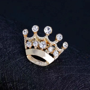 Detailed close-up of golden crown brooch with sparkling rhinestones on black fabric