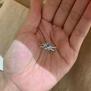 Close-up of a silver criss-cross ring featuring a light blue gemstone and twisted texture