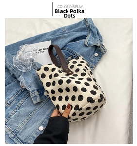 Detailed close-up of cream canvas bucket bag with black polka dots and brown leather handle