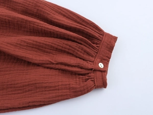Detail of reddish-brown textured cotton fabric with pleated cuffs and a small white button