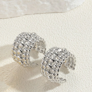 Detail of silver beaded ear cuff with bubbly metallic texture on a white stone background