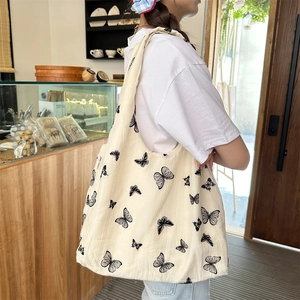 Close-up of a cream canvas tote bag featuring black butterfly patterns and woven texture