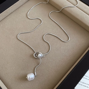 Detailed macro view of a silver snake chain necklace featuring a round pearl and metal ring