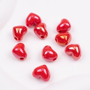 Close-up of small red heart-shaped ceramic beads for DIY jewelry making on a white plate