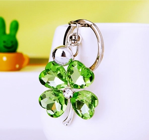 Close-up of a silver keychain featuring green crystal four-leaf clover on a ceramic base