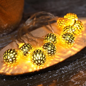 Golden hollow metal LED globe string lights on wood with warm yellow festive lighting