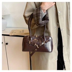 Detail of dark brown glossy leather handbag with gold buckle and zipper on beige trench coat