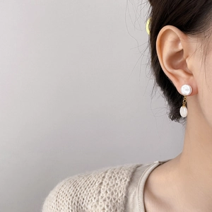Detail of elegant double pearl earrings with gold connectors on a model in beige knitwear