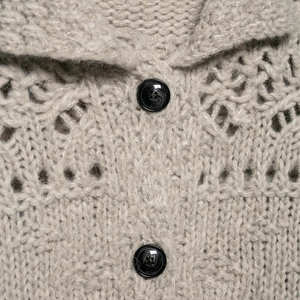 Close-up of hollow out knit cardigan with textured black buttons in light taupe