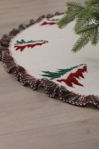 Close-up of white knitted Christmas tree skirt with red and green cedar patterns and fringe