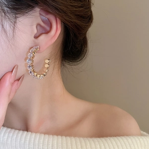 Detail shot of a model wearing a gold C-shaped earring inlaid with sparkling rhinestones