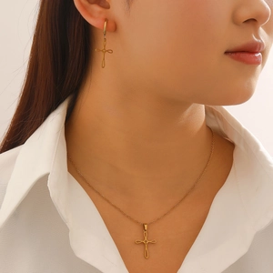 Close-up of a model wearing a minimalist gold cross necklace and matching earrings set