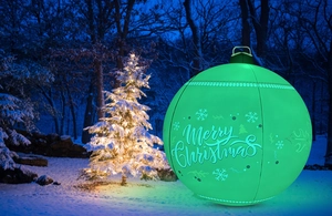 Illuminated 60cm green inflatable Christmas ball with Merry Christmas print in a snowy forest