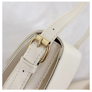 Close-up of golden metal buckle and stitching on white leather crossbody bag strap