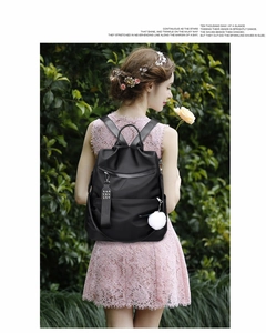 Close-up of black nylon backpack with a white fluffy pompom charm and floral background