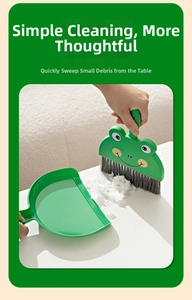 Detailed view of hand using green frog-themed mini broom and dustpan for desk cleaning