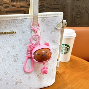 Adorable pink Capybara keychain with rotating face hanging on a white textured handbag