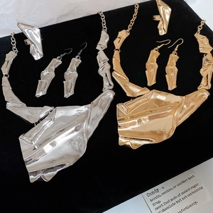 Detailed view of irregular crinkled metal necklaces and jewelry set on a black display