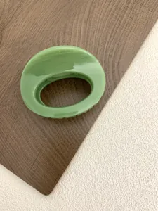 Detail view of a glossy grass green oval hollow hair claw clip on a textured background