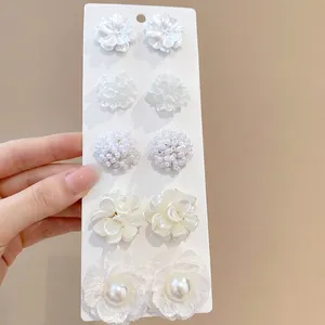 5-pair set of elegant white floral earrings with pearls and lace on a display board