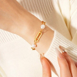 Detail of gold chain and freshwater pearl bracelet worn on wrist with white sweater