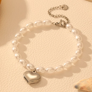 Détail d'un pendentif cœur argenté et de perles blanches sur un bracelet en acier inoxydable