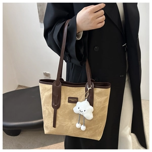Detail of khaki canvas tote bag with brown leather straps and cloud plush charm