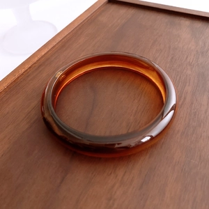 Detail of amber acrylic bangle with polished surface on a dark wood grain tray background