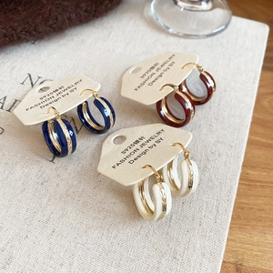 Close-up of enamel hoop earrings in navy blue, burgundy, and cream on a vintage background